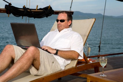 Man on deck of yacht with laptop